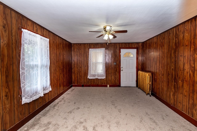 carpeted spare room featuring wood walls, baseboards, radiator, and ceiling fan