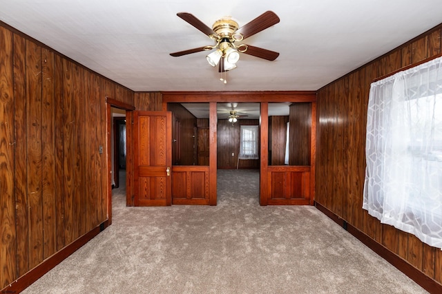 carpeted spare room with wood walls, baseboards, and a ceiling fan