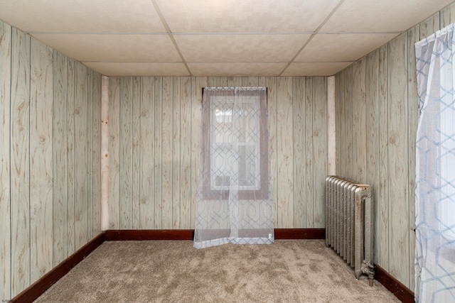 carpeted spare room featuring a paneled ceiling, baseboards, and radiator