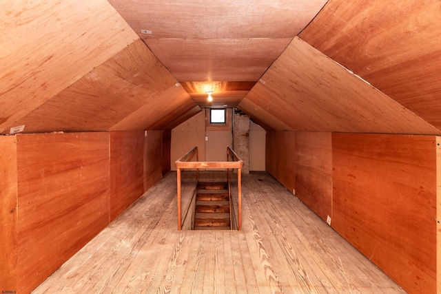 bonus room with wood walls, light wood finished floors, and vaulted ceiling
