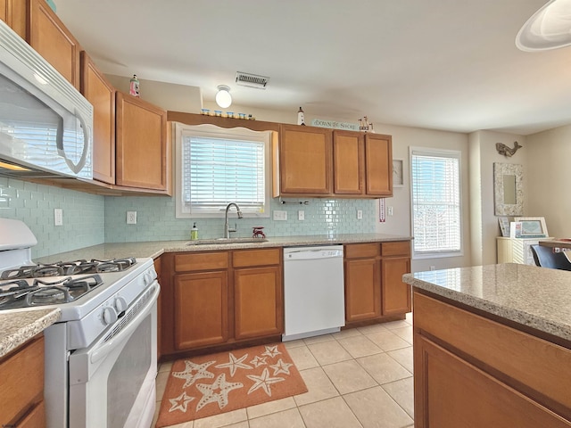 kitchen featuring a sink, white appliances, brown cabinetry, backsplash, and light tile patterned flooring