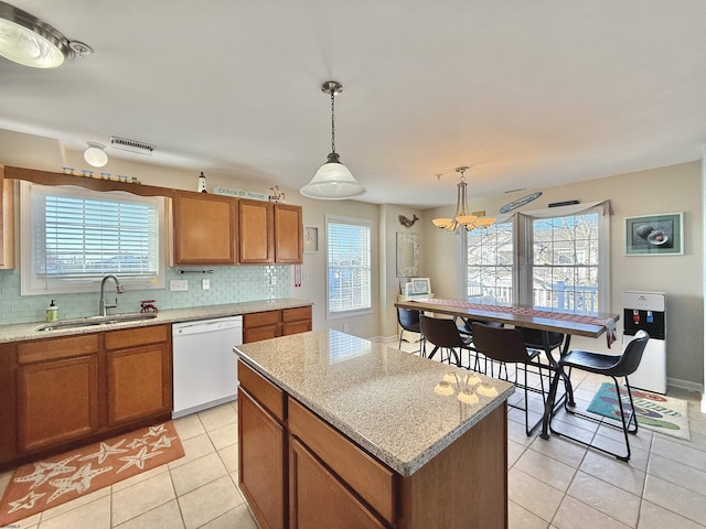 kitchen with light tile patterned floors, brown cabinetry, decorative backsplash, white dishwasher, and a sink