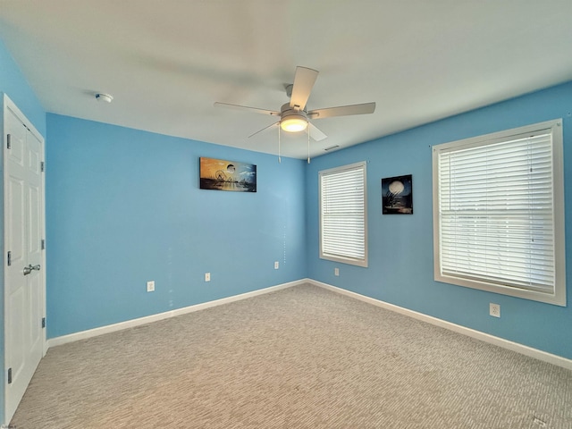 carpeted spare room featuring ceiling fan and baseboards