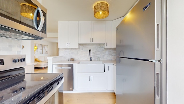 kitchen featuring white cabinetry, light countertops, a sink, stainless steel appliances, and decorative backsplash