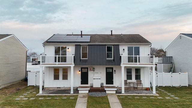 view of front of property with fence, roof mounted solar panels, a gate, and a balcony