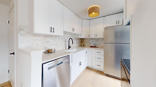 kitchen featuring light countertops, a sink, stainless steel appliances, light wood finished floors, and backsplash
