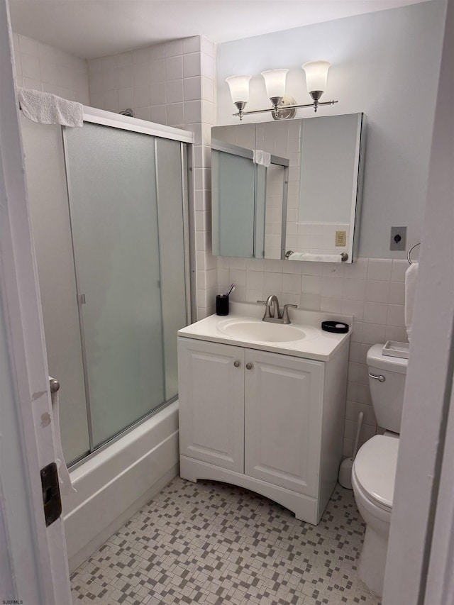 bathroom featuring a shower with door, vanity, tile patterned floors, toilet, and tile walls