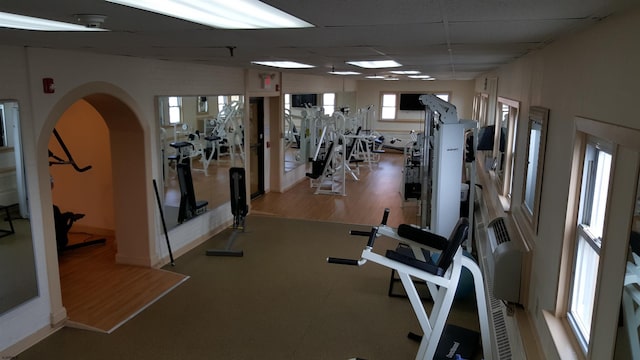 workout area with arched walkways, wood finished floors, and a paneled ceiling
