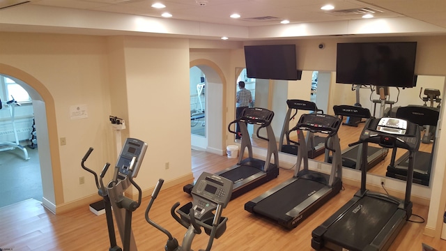 exercise room with baseboards, light wood-type flooring, arched walkways, and recessed lighting