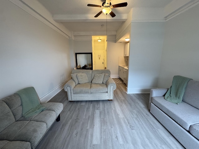 living area with beamed ceiling, light wood-style flooring, baseboards, and a ceiling fan