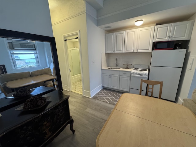 kitchen featuring a sink, white cabinetry, white appliances, and wood finished floors