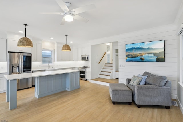 kitchen featuring white cabinets, stainless steel appliances, light countertops, a sink, and a center island