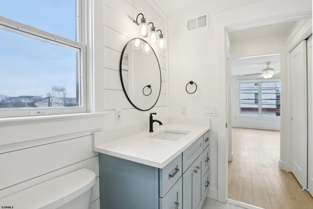 half bath with a ceiling fan, wood finished floors, vanity, toilet, and visible vents