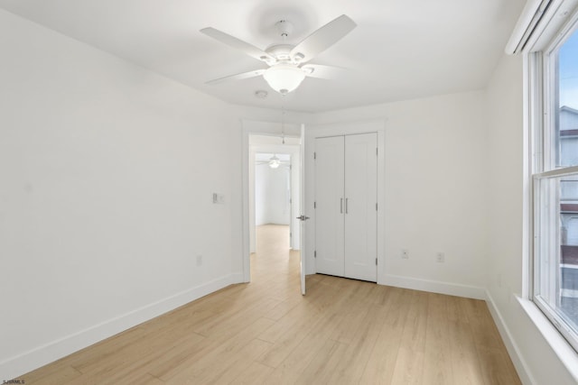 spare room featuring a ceiling fan, baseboards, light wood-style floors, and a healthy amount of sunlight