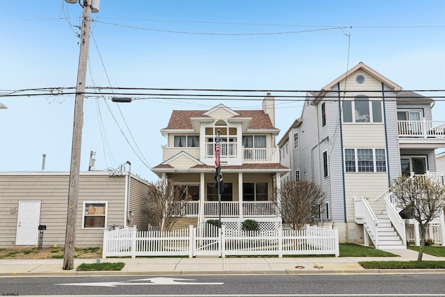 victorian-style house featuring stairway, a porch, a balcony, and a fenced front yard