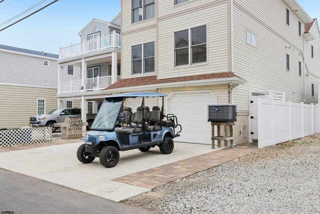 view of front facade with an attached garage, a balcony, concrete driveway, and fence