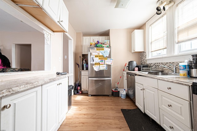 kitchen featuring light wood finished floors, stainless steel appliances, a sink, and white cabinetry