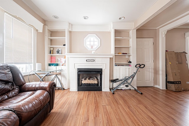 living room with a fireplace, light wood-style flooring, built in shelves, and recessed lighting