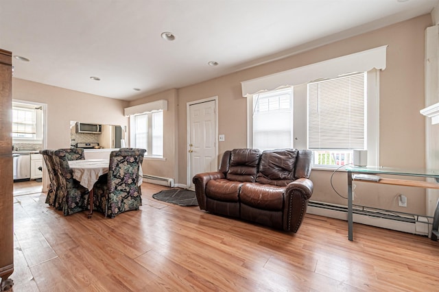 living area featuring a baseboard heating unit, light wood-style floors, and a healthy amount of sunlight