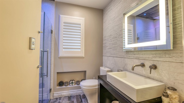 bathroom with wood finished floors, toilet, vanity, tile walls, and a stall shower