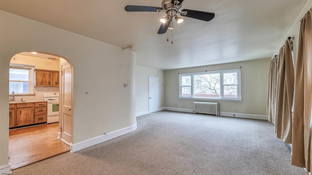 spare room with a ceiling fan, radiator heating unit, plenty of natural light, arched walkways, and light carpet