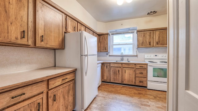 kitchen featuring visible vents, white appliances, a sink, and brown cabinets