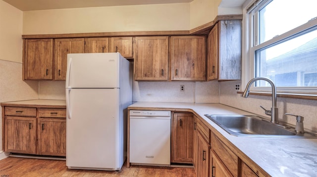kitchen featuring brown cabinets, a sink, white appliances, and light countertops