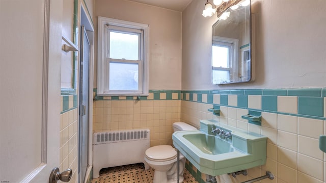 half bath featuring radiator heating unit, a healthy amount of sunlight, toilet, and tile walls