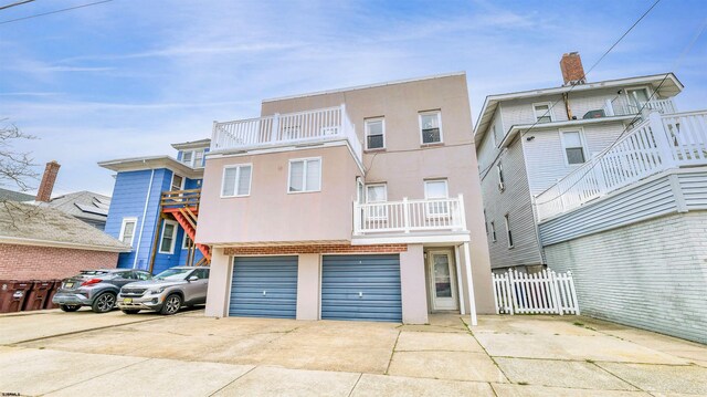 view of property with a balcony, concrete driveway, an attached garage, fence, and stucco siding