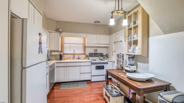 kitchen with light countertops, wood finished floors, a sink, white appliances, and glass insert cabinets