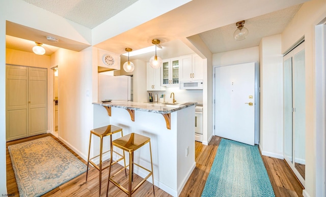 kitchen with white appliances, glass insert cabinets, a kitchen bar, white cabinetry, and a peninsula