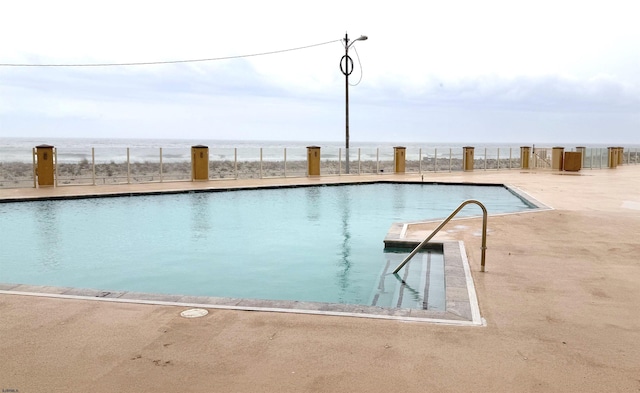 pool with a patio, a water view, and fence