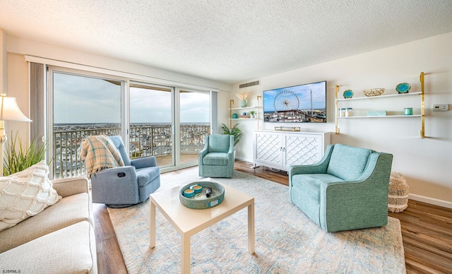 living area with a textured ceiling, visible vents, wood finished floors, and baseboards