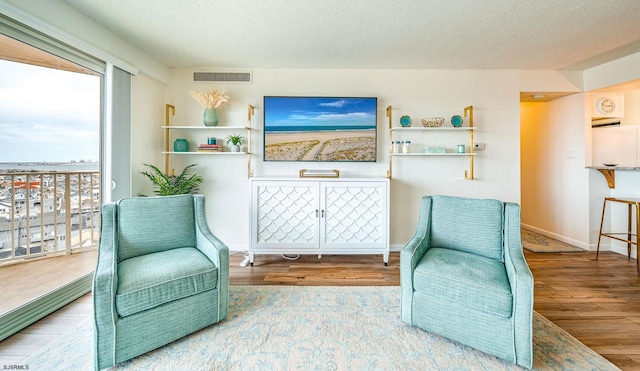 sitting room with a textured ceiling, wood finished floors, visible vents, and baseboards