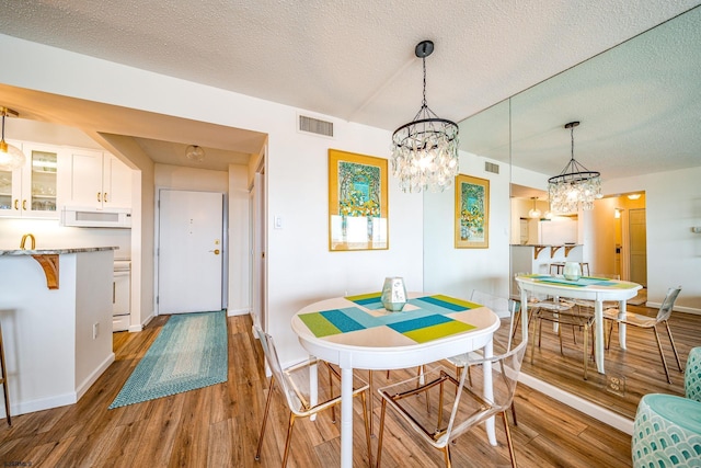 dining area with a textured ceiling, visible vents, a notable chandelier, and light wood-style floors
