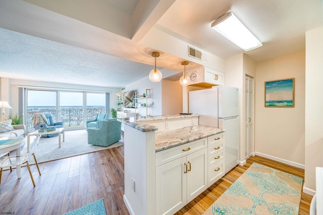 kitchen featuring light stone counters, freestanding refrigerator, light wood-style floors, white cabinets, and open floor plan