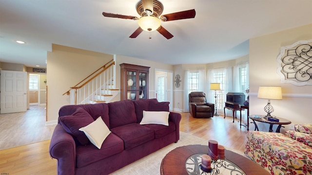 living area with light wood-style floors, a wealth of natural light, stairs, and ceiling fan