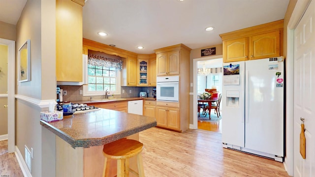 kitchen featuring a breakfast bar, a sink, white appliances, a peninsula, and tasteful backsplash