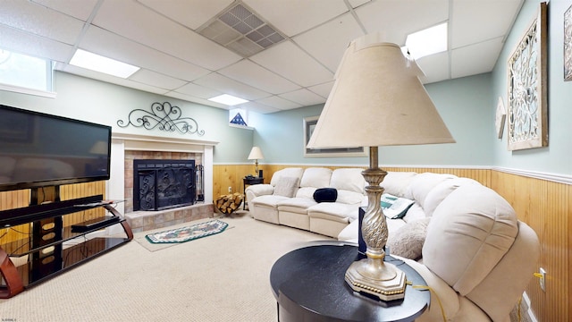 carpeted living room featuring wainscoting, a fireplace, visible vents, and a paneled ceiling