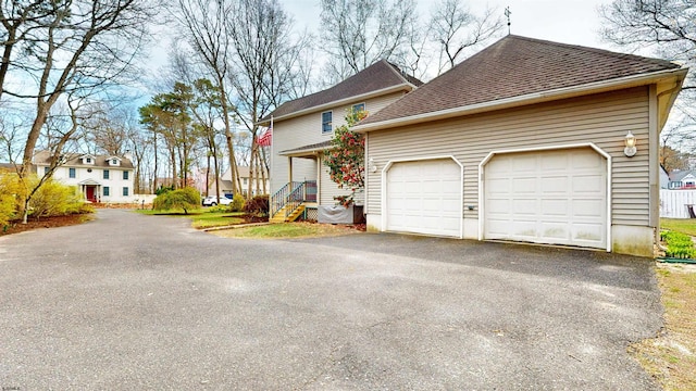 view of side of home featuring a garage, driveway, and roof with shingles
