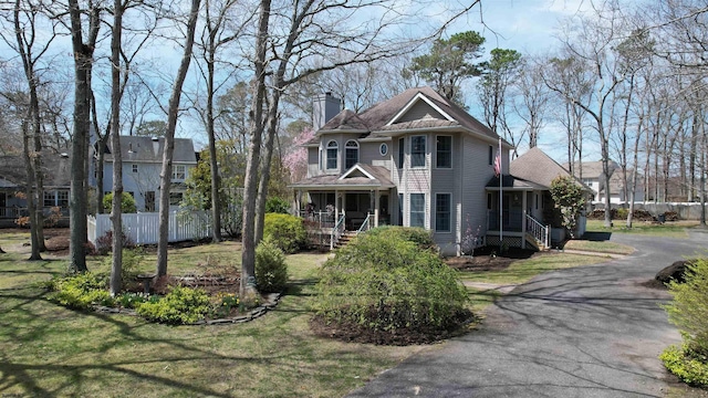 victorian house with aphalt driveway, a chimney, and covered porch