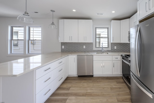 kitchen with light wood finished floors, a sink, a peninsula, appliances with stainless steel finishes, and white cabinetry