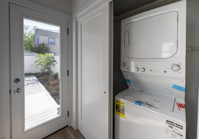 clothes washing area with stacked washer / drying machine, wood finished floors, and laundry area