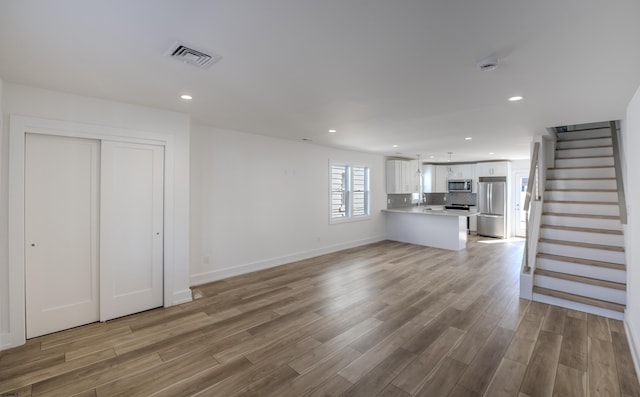 unfurnished living room featuring recessed lighting, light wood-type flooring, visible vents, and stairway