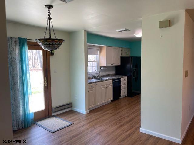 kitchen with wood finished floors, a sink, a baseboard heating unit, baseboards, and black appliances