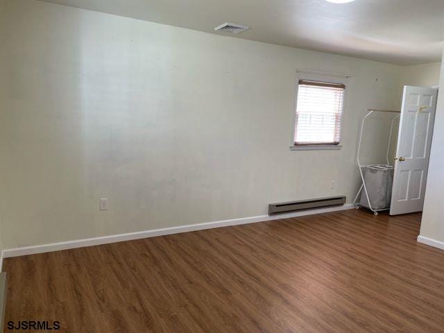 empty room featuring visible vents, baseboards, wood finished floors, and a baseboard radiator