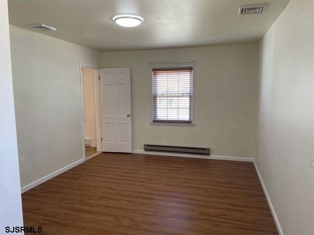 empty room featuring a baseboard radiator, wood finished floors, visible vents, and baseboards
