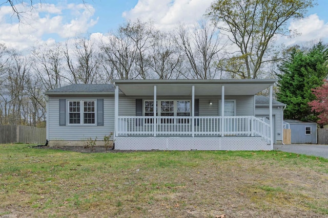 single story home featuring covered porch, fence, an outbuilding, a front yard, and a storage unit
