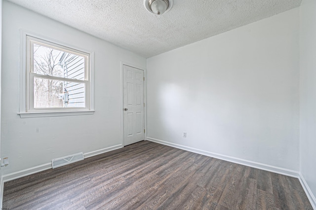 spare room featuring baseboards, dark wood-type flooring, visible vents, and a textured ceiling