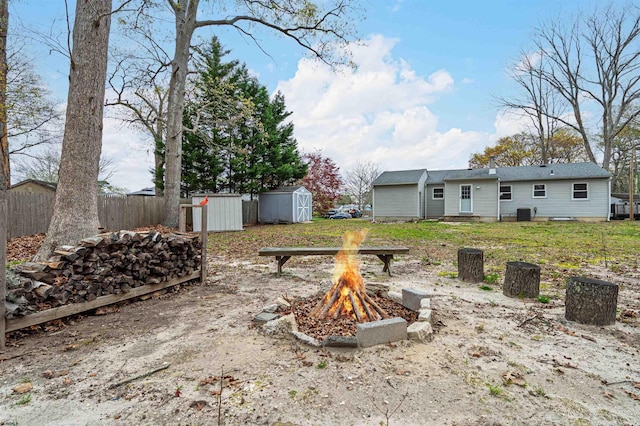 view of yard featuring fence, a storage shed, central AC, an outbuilding, and an outdoor fire pit